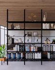 Floor-to-ceiling room divider shelving unit with white shelves and white vertical posts, 3 bays, 31-inch bay width, six open shelf levels, floor-to-ceiling supports, styled in a room setting with books and decor.