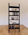 Floor-to-ceiling room divider shelving unit with lower storage cabinets with black shelves and black vertical posts, 31-inch bay width, six open shelf levels, floor-to-ceiling supports.