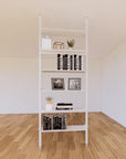 Floor-to-ceiling room divider shelving unit with lower storage cabinets with white shelves and white vertical posts, 31-inch bay width, six open shelf levels, floor-to-ceiling supports.