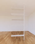 Floor-to-ceiling room divider shelving extension with lower storage cabinet with white shelves and white vertical post, one bay, 31-inch bay width, six open shelf levels, floor-to-ceiling supports.