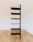 Floor-to-ceiling room divider shelving extension with lower storage cabinet with black shelves and black vertical post, one bay, 24-inch bay width, six open shelf levels, floor-to-ceiling supports.