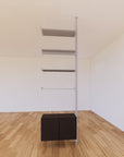 Floor-to-ceiling room divider shelving extension with lower storage cabinet with black shelves and satin vertical post, one bay, 24-inch bay width, six open shelf levels, floor-to-ceiling supports.