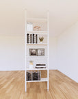 Floor-to-ceiling room divider shelving extension with lower storage cabinet with white shelves and white vertical post, one bay, 24-inch bay width, six open shelf levels, floor-to-ceiling supports.