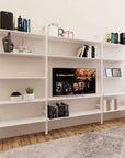 Modular media shelving unit with white shelves and black vertical posts, one bay, styled as an entertainment storage unit.