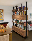 Floor-to-ceiling room divider shelving unit with lower storage cabinets with Casting Light shelves and white vertical posts, one bay, 24-inch bay width, six open shelf levels, floor-to-ceiling supports, styled in a room setting with books and decor.