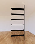 Floor-to-ceiling room divider shelving extension with lower storage cabinet with black shelves and black vertical post, one bay, 31-inch bay width, six open shelf levels, floor-to-ceiling supports.