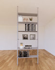 Floor-to-ceiling room divider shelving unit with lower storage cabinets with satin shelves and satin vertical posts, 31-inch bay width, six open shelf levels, floor-to-ceiling supports.