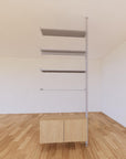 Floor-to-ceiling room divider shelving extension with lower storage cabinet with Casting Light shelves and satin vertical post, one bay, 31-inch bay width, six open shelf levels, floor-to-ceiling supports.