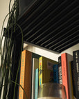 Floor-to-ceiling room divider shelving unit with white shelves and black vertical posts, one bay, 24-inch bay width, six open shelf levels, floor-to-ceiling supports, styled in a room setting with books and decor.