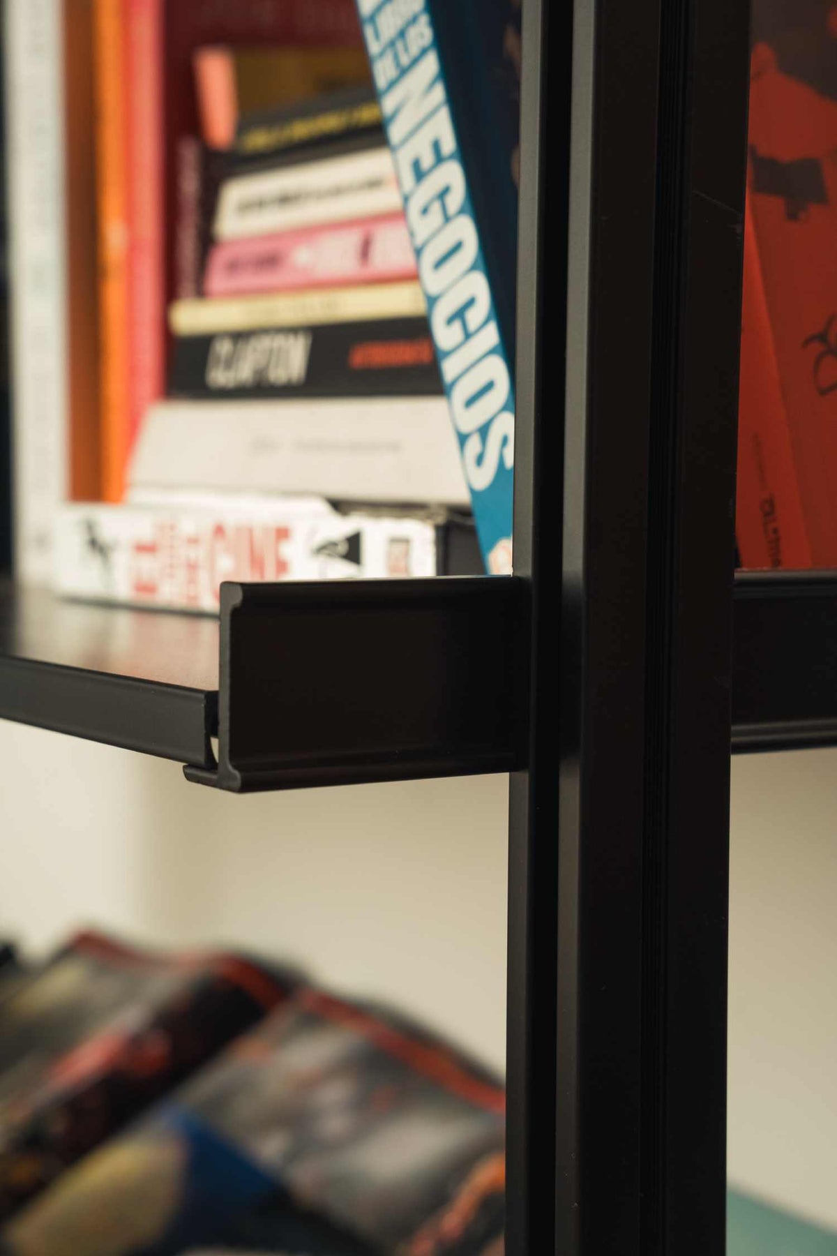 Floor-to-ceiling room divider shelving unit with black shelves and white vertical posts, one bay, 24-inch bay width, six open shelf levels, floor-to-ceiling supports, styled in a room setting with books and decor.