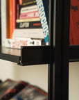 Floor-to-ceiling room divider shelving unit with black shelves and white vertical posts, one bay, 24-inch bay width, six open shelf levels, floor-to-ceiling supports, styled in a room setting with books and decor.