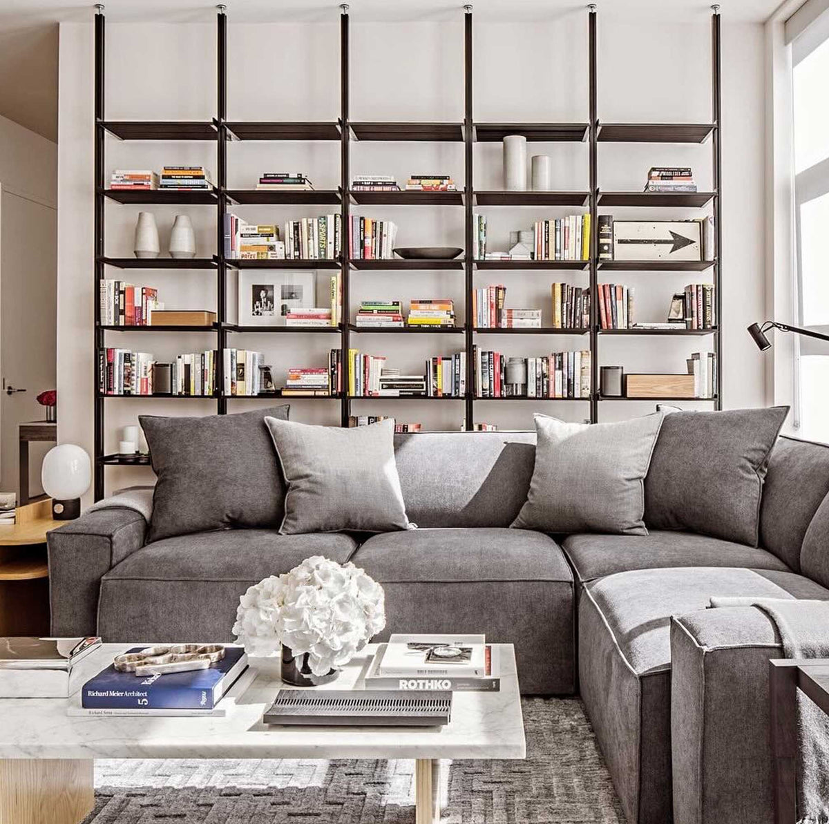 Floor-to-ceiling room divider shelving unit with black shelves and black vertical posts, one bay, 24-inch bay width, six open shelf levels, floor-to-ceiling supports, styled in a room setting with books and decor.